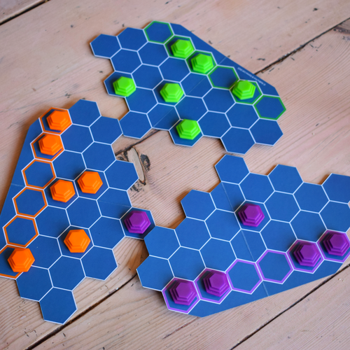 ButtChess + 1 game board arranged with orange, green and purple playing pieces on a wooden table, showcasing a compact travel board game and affordable abstract strategy game for easy play on the go.