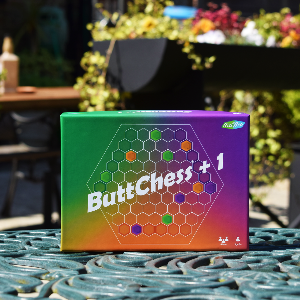 ButtChess +1 game box displayed outdoors on a garden table, highlighting its compact travel-friendly design and £13.99 price for affordable three-player strategy games on the go.
