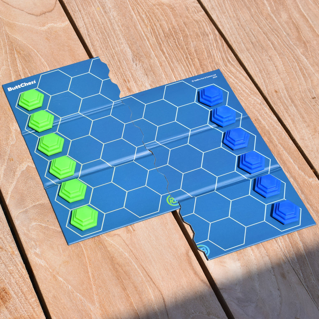 ButtChess travel board game set up outdoors on a wooden table, showing blue and green playing pieces on a portable hexagonal game board. An easy-to-learn, replayable strategy board game for all ages, ideal for holidays, travel, family game nights and affordable gaming under £20.