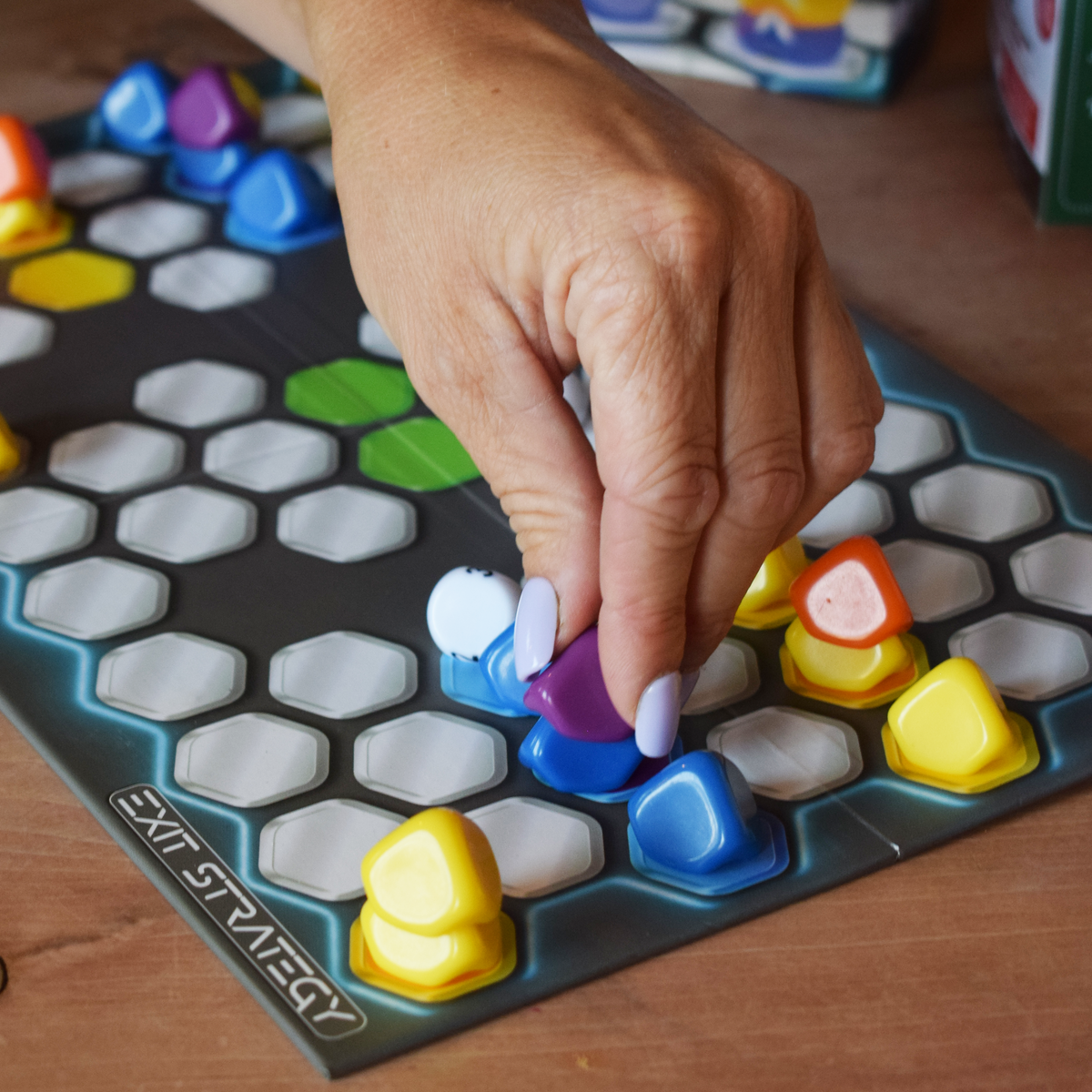 Exit Strategy board game in action, with a player moving colourful counters across the hexagonal space-themed board, showcasing tactical gameplay, quick-play abstract strategy and a compact travel game for two players.